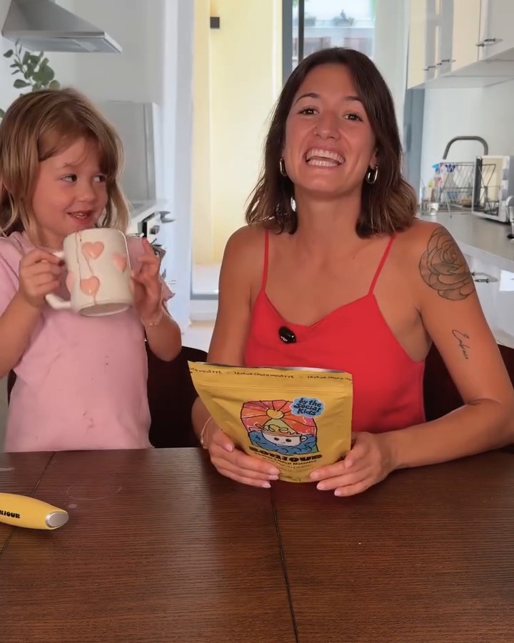 A mother and her young daughter at the kitchen table, the daughter holding a mug of chocolate drink
