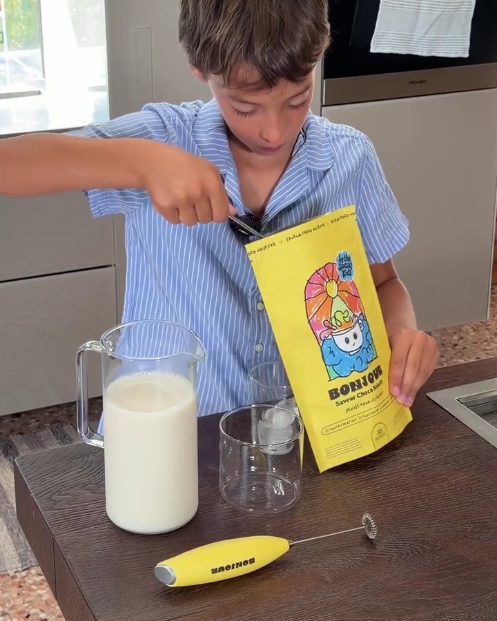 A boy spooning Bonjour Kids powder from the pouch into a glass, with a jug of milk beside him